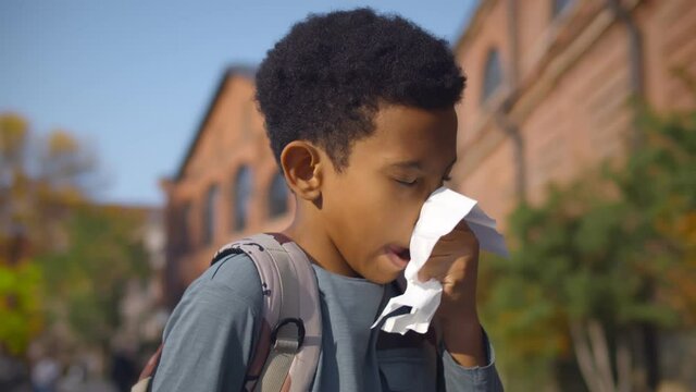 Portrait of african schoolboy sneezing and wipes nose with napkin outdoors