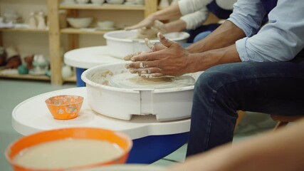 Tilt up closeup side view shot of hands of three diverse pottery artists throwing pots on wheels in ceramic art studio