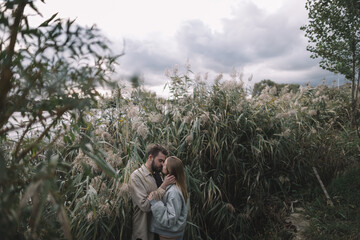 a loving couple stands in the reeds against the backdrop of a lake in the evening and communicates