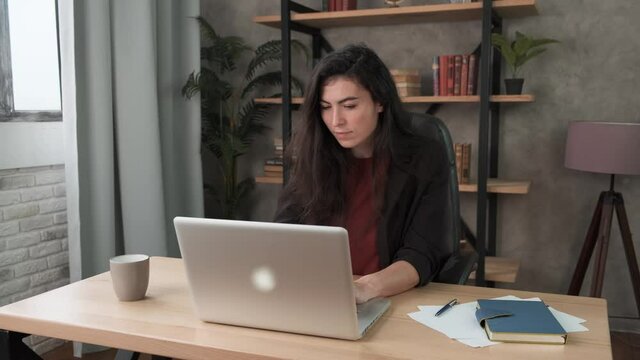 Young woman employee in the office at the computer. Brunette girl fills out a questionnaire or resume, takes a test on a laptop. Work during self-isolation and quarantine COVID-19 4k