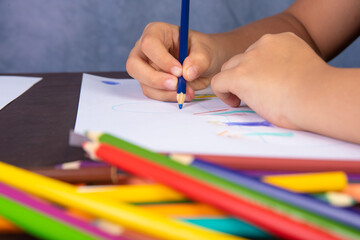 Hands of a child drawing with colored pencils, gray background, selective focus.