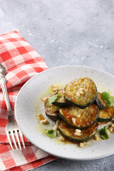 Fried zucchini slices with pine nuts and coriander in a light plate on a gray background. Fork and red cloth. Restaurant menu. Background image, copy space