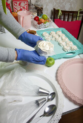 A woman in a medical mask and rubber gloves makes a marshmallow rose at home. Marshmallow on a tray, around the tools for its preparation. Cooking sweets during a pandemic.