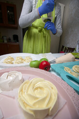 A woman in rubber gloves and a medical mask makes homemade marshmallows. Fresh marshmallows are nearby on a tray. Cooking sweets during a pandemic.