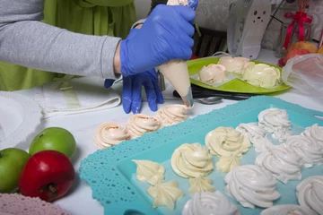 Foto op Canvas A woman in rubber gloves and a medical mask makes homemade marshmallows. Fresh marshmallows are nearby on a tray. Cooking sweets during a pandemic. © f2014vad