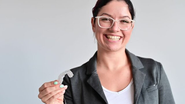 The woman smiles and holds a transparent plastic orthodontic device for bite correction