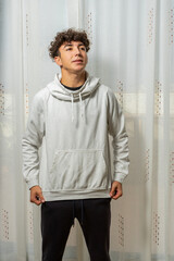 Attractive young man with curly hair wearing white sweatshirt posing on white curtains background