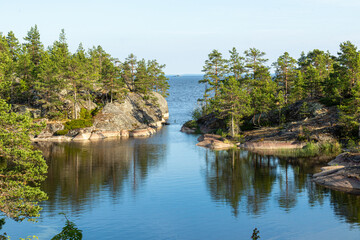 beautiful landscape of green, natural trees, plants, stones on an island surrounded by a natural reservoir, lake against a blue sky in Karelia, Russia