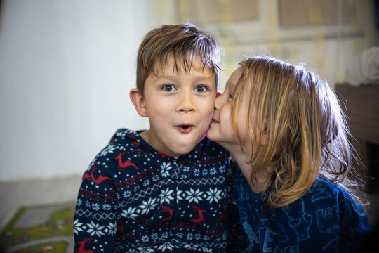 Two siblings in pajamas with book, sister kiss brother, funny emotions huge home