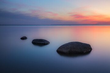 Fototapeta na wymiar Stones on sea coast. Sunset over the sea. Deep blue color of summer late sunset. Long exposure