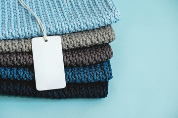 Stack of knitted material from threads of dark blue, light blue, gray colors with blank Price Tag on a blue background. Copy, empty space for text