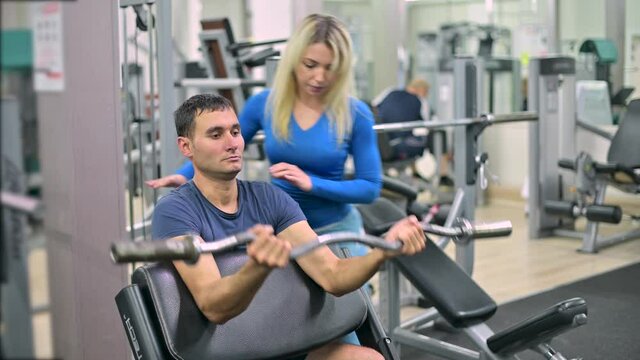 Skinny guy doing biceps exercise under the supervision of a trainer in a gym. Training under the supervision of a trainer in a fitness club