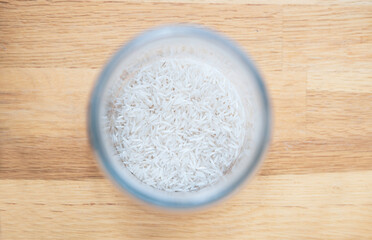 White long-grain basmati rice, jasmine in a glass jar on a wooden oak tabletop background top view. Ideas for storing bulk food, cereals at home in the kitchen.