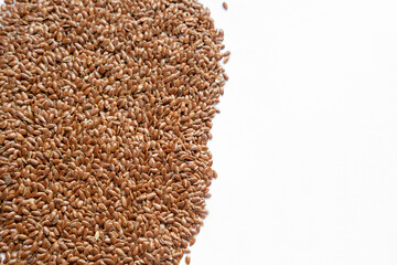 A lot of scattered brown clean flax seeds on a white background on the left and copy space on the right. Vegetarian and healthy food.