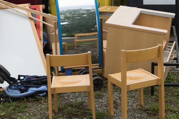 Bulky waste, old chairs and tables of the classroom in a school building, placed in the natural environment, waiting for the removing