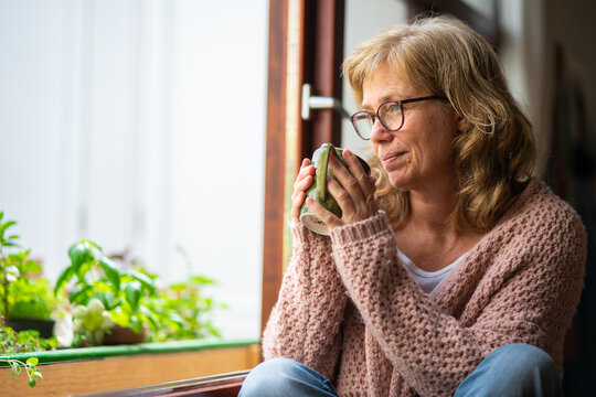 Adult woman taking tea pensive looking out the window