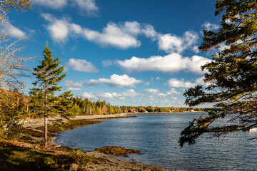 Maine shoreline under a fall sky with billowing clouds and colorful autumn shoreline of Hancock Point.
