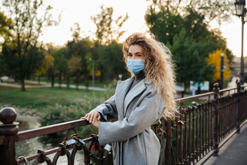 A young woman in a protective mask stands on the bridge