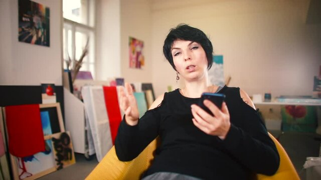 A woman with a phone in her hands is talking while sitting. Give interviews to inform viewers. Communication using media.