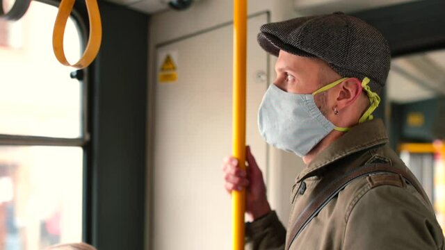 A man wearing a mask rides on public transport, looks out the window. Transportation of passengers in the city. Respiratory protection rule in a public place.