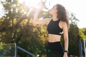 Young woman drinking water after training in park