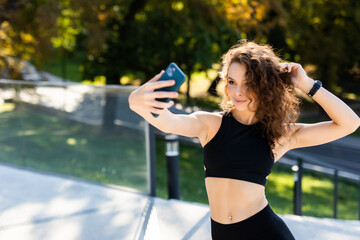 Selfie time. Young athletic woman with perfect body in sportswear making selfie by her smart phone in the city park.