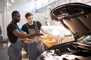 two friendly professional auto mechanic during work, they are successfully repairing car, solve problems together