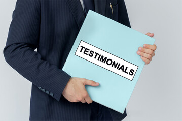 A businessman holds a folder with documents, the text on the folder is - TESTIMONIALS