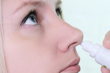 A woman with a runny nose holds a medicine in her hand, nasal spray irrigations to stop allergic rhinitis and sinusitis