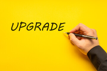 Male hand writes in black pen the word upgrade on a yellow background with copy space. Business...