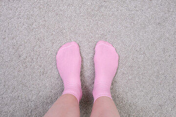 Woman female legs wearing pink plain cotton socks of classic style with elastic band standing on a cozy carpet at home