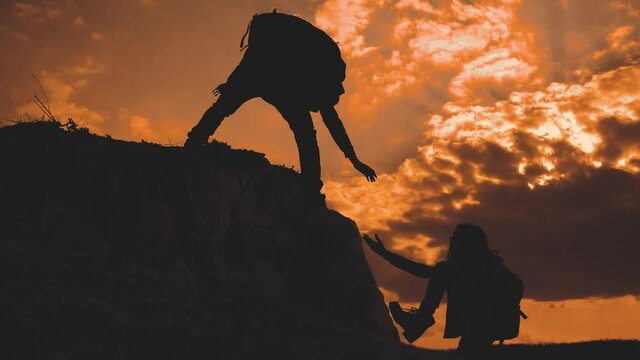 teamwork help business travel silhouette at sunset sunlight slow motion video concept. man and girl holds out a helping hand mutual assistance camping adventure a pair of hikers climb lifestyle a