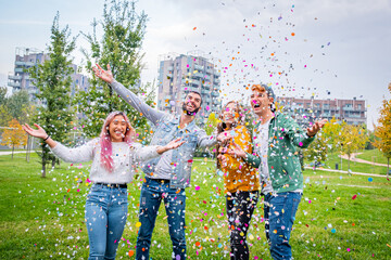Group of stylish friends smiling and enjoying party throwing colorful confetti to the sky -...