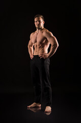 Strong athletic man showes naked muscular body on a dark background.