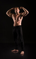 Fototapeta na wymiar Strong athletic man showes naked muscular body on a dark background.