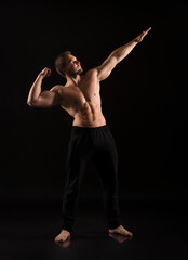 Fototapeta na wymiar Strong athletic man showes naked muscular body on a dark background.