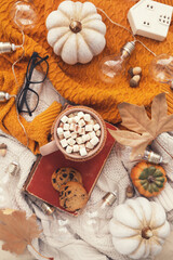 Cup of coffee with marshmallows, pumpkins, dry leafs, acorns, light bulbs and knitted sweaters