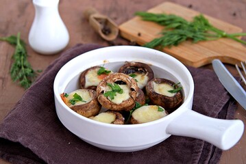 Hot appetizer, baked mushrooms with suluguni cheese in white ceramic form.