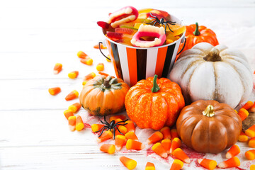 Halloween pumpkins and candies in bucket on white wooden background