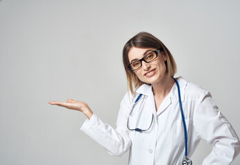 woman nurse in a medical gown gesturing with her hands on a light background copy space