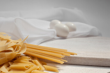 Variety of pasta pasta, three eggs on top of wood and white fabric with breathing area for commercial use.