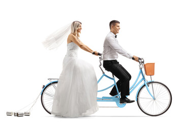Full length profile shot of a bride and groom riding on a tandem bicycle