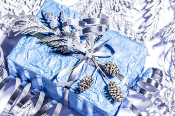 Christmas presents with handmade gift box in silver blue color decorated with pine cones and twigs on white background, preparation for holidays. Selective focus