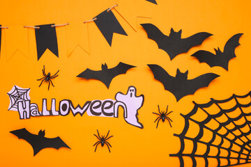 Word Halloween with paper bats, ghost, spiderweb, flags and spiders on orange background