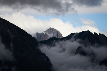 Dramatic dolomite rock between clouds with green forest below