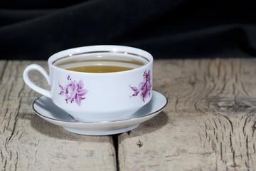 The tea in a beautiful white floral tea cup is placed on an old wooden table