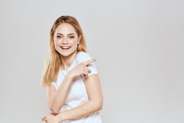 cheerful blonde in a white t-shirt gesturing with her hands light background