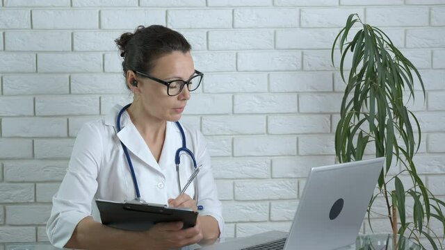 Record patient complaints. A nice smart doctor in a coat listen the patient online and write the symptoms on paper.