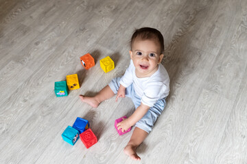 Baby is playing with blocks. A little boy in white bodysuit at home. Beautiful portrait of a toddler. Big-eyed baby. Remote education. Distance learninig

