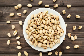 Tasty pistachios in plate on wooden table